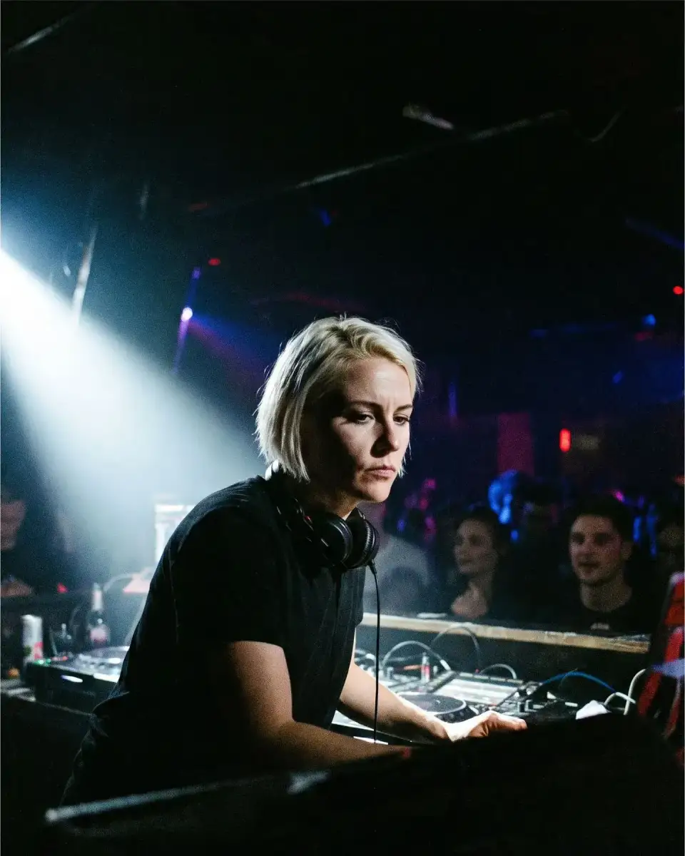 Porträt von Mika Sturm am DJ-Pult, kurze helle Haare, Kopfhörer um den Hals