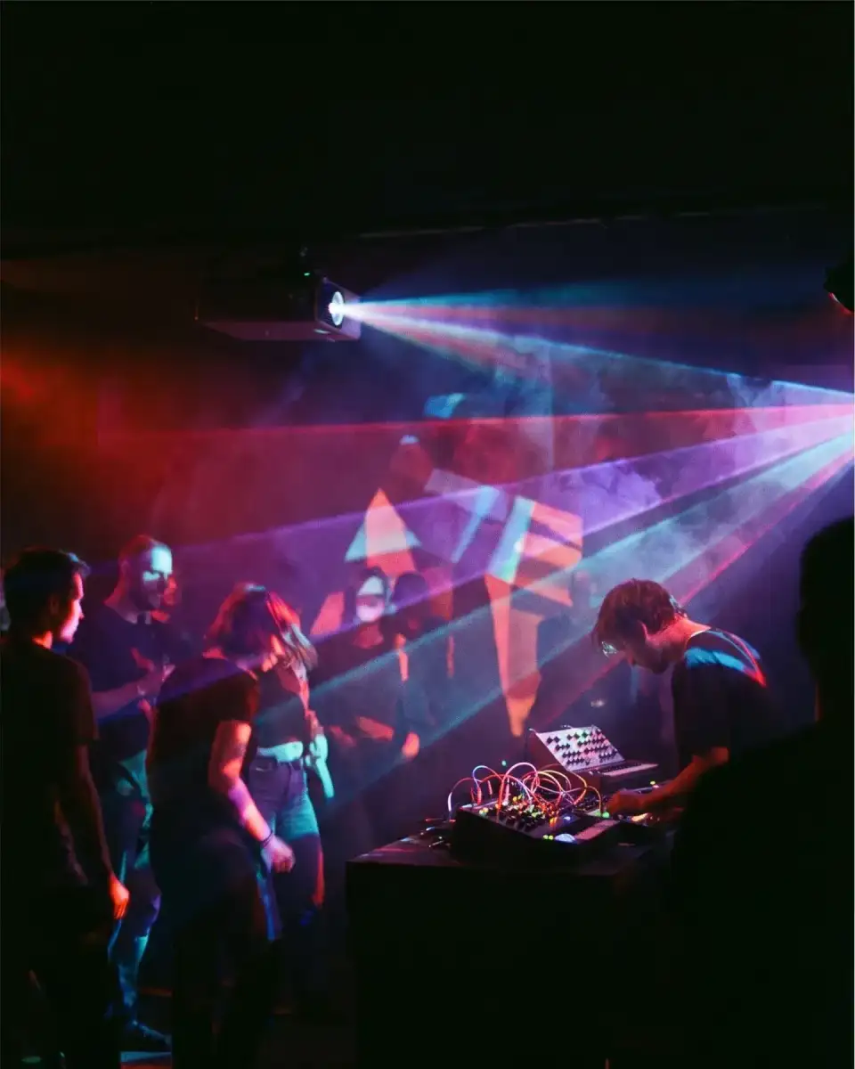 Artwork Kunstlicht: farbige Lichtmuster über dem Publikum, rechts ein Musiker an Synthesizern